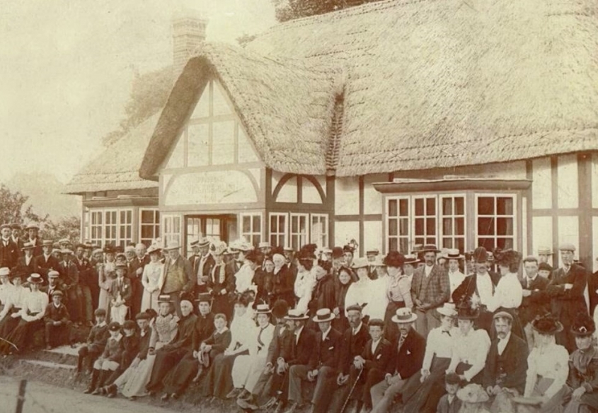 Black and white photo of group of people sitting outside Village Hall